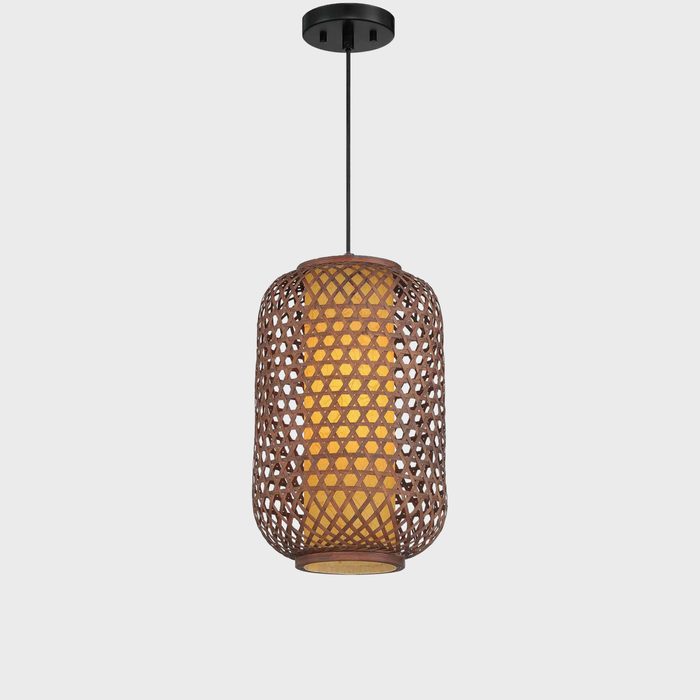 A woven pendant lamp hangs from the ceiling, casting a warm glow through its patterned structure, illuminating a plain, light-colored background.