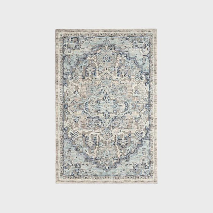 A patterned rug displays intricate designs in blue, beige, and cream, resting against a neutral background, enhancing the room’s aesthetic with its ornate detailing.