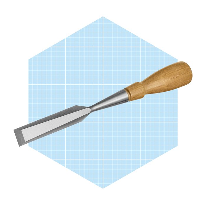 A chisel rests diagonally on a light blue grid-patterned background, featuring a metal blade and a wooden handle, suggesting woodworking or carving use.