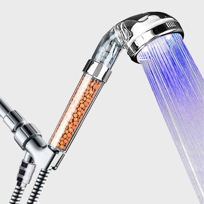 A showerhead dispenses water with blue lighting, featuring a transparent section filled with orange beads, suggesting a water filtration system.