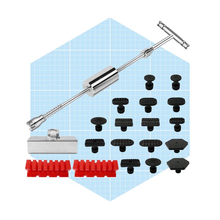 A metal dent repair tool rests alongside various black and red rubber attachments on a light blue grid background, designed for vehicle bodywork repair.