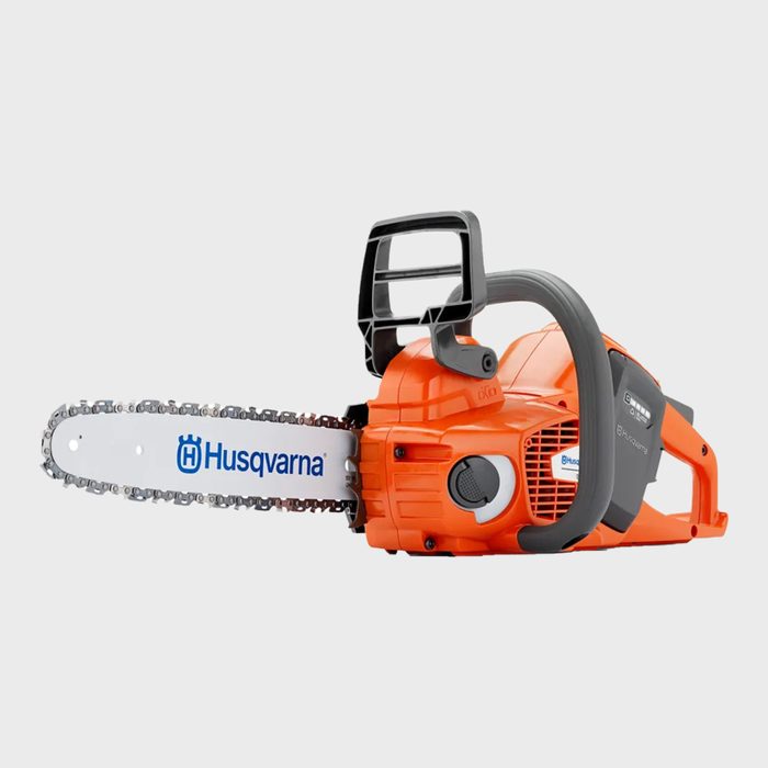 An orange chainsaw rests horizontally, featuring a metal blade with a logo. It's designed for cutting wood in outdoor environments.