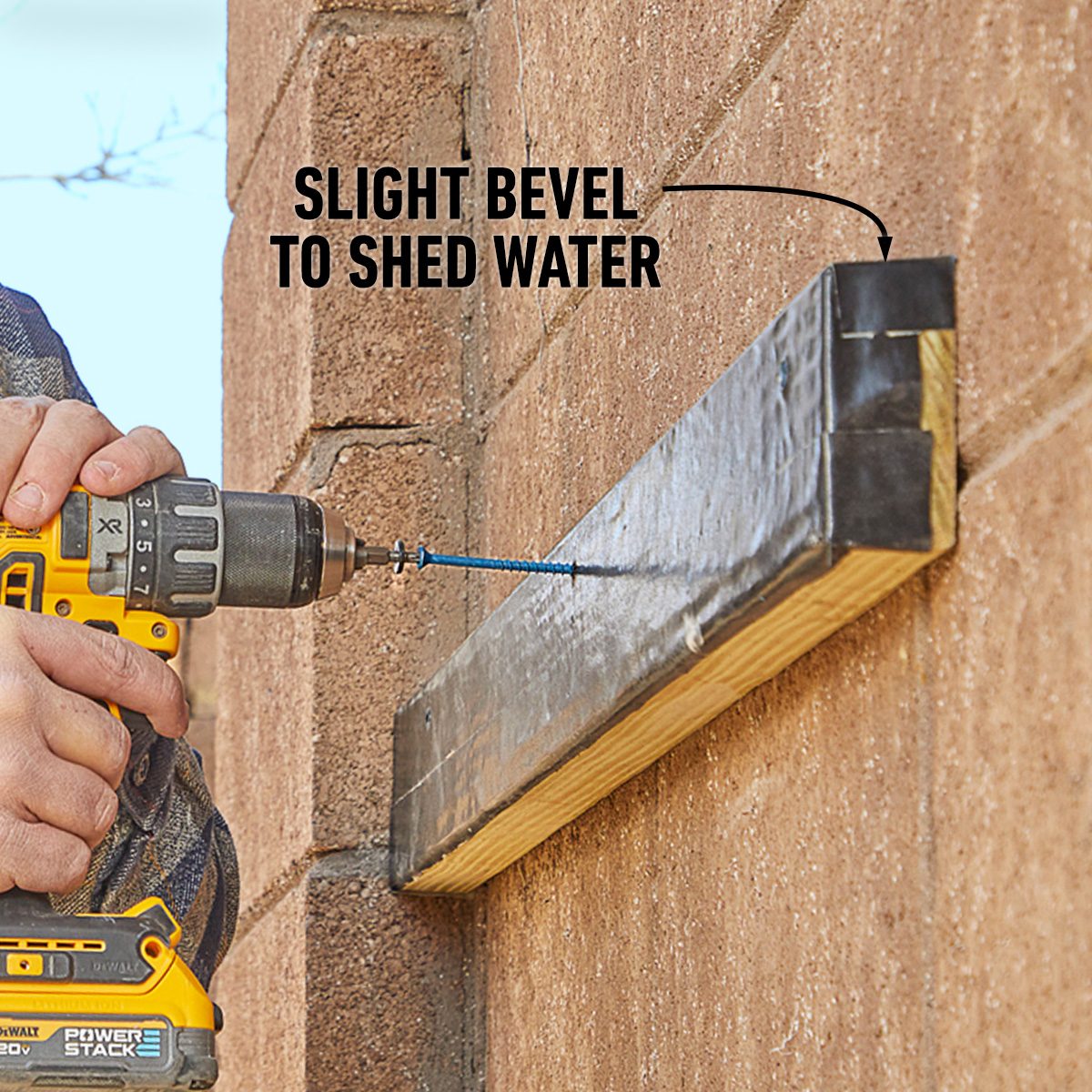 A person uses a power drill to attach a wooden beam to a brick wall, ensuring a slight bevel for water drainage.