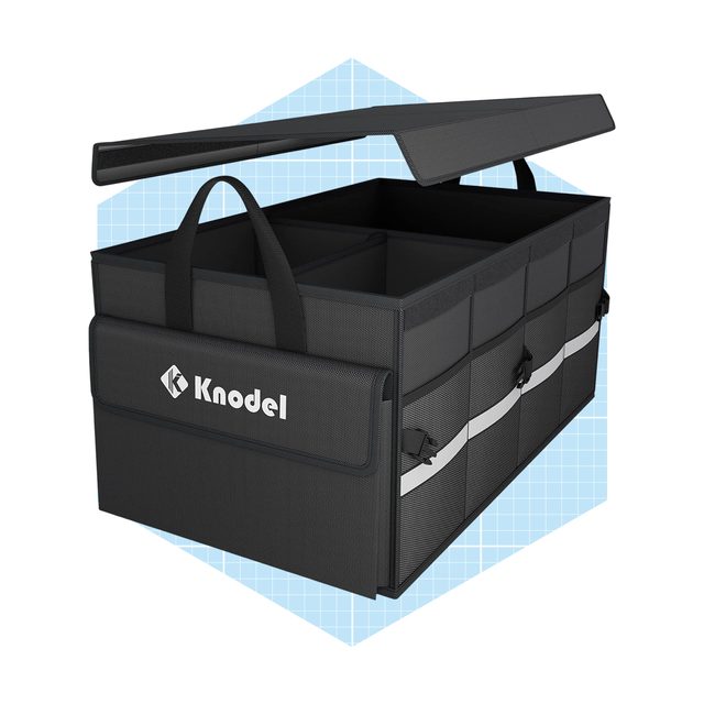 A rectangular storage bin with a lid is open, revealing multiple compartments inside. It's dark gray with a logo and is set against a blue grid background.