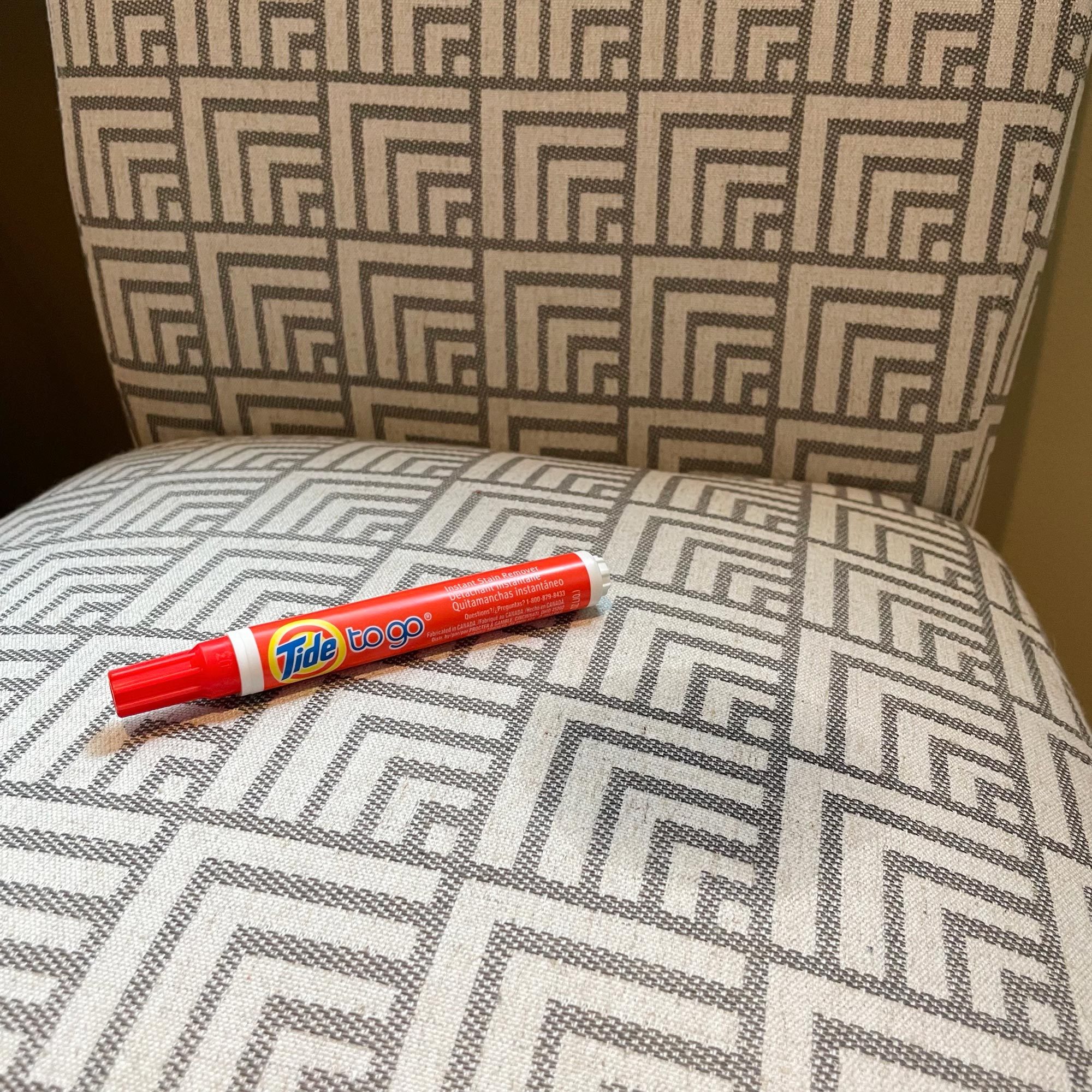 tide to go pen resting on an upholstered dining room chair next to a wet spot where a stain has been removed