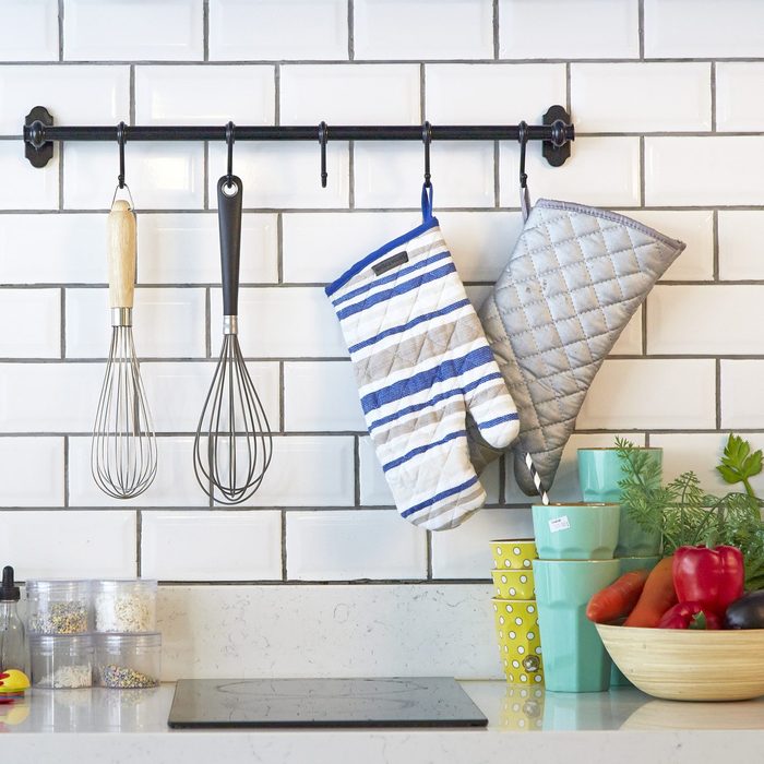 Modern kitchen with utensils and oven mitts hanging from a curtain rod