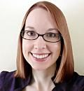 A person with short, straight red hair smiles while wearing glasses, set against a plain light-colored background.