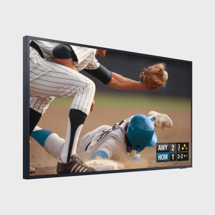 A baseball player slides into home plate to avoid a tag, while the opposing player reaches out with a glove. A scoreboard shows the game status.