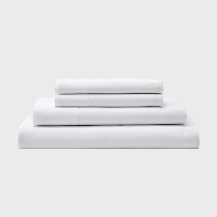 Four neatly stacked white bed sheets of varying sizes are arranged against a plain gray background, creating a clean and minimalist aesthetic.