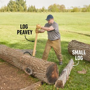 A person uses a log peavey to lift a large log in a grassy outdoor area, surrounded by additional logs and trees in the background.
