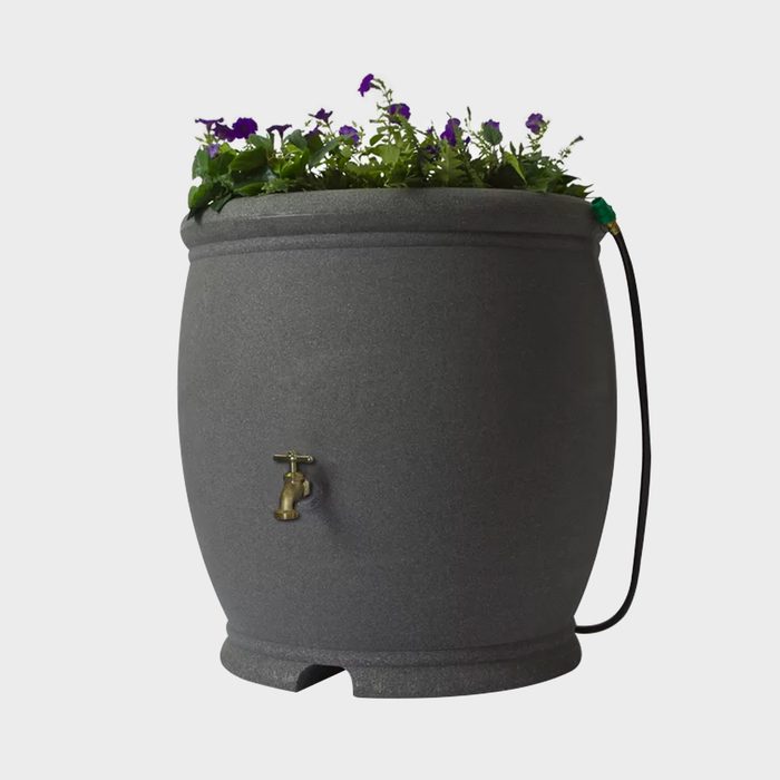 A gray rain barrel with a brass faucet contains blooming purple flowers, situated in a neutral background, promoting eco-friendly gardening.