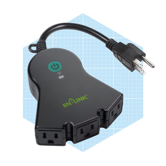 A black power strip has three outlets and a power button; it's connected to a plug and set against a light blue grid background.