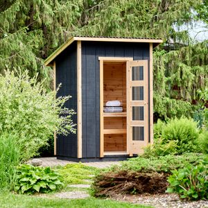 A small, wooden storage shed stands in a garden, its door ajar revealing shelves with towels, surrounded by lush greenery and pathways.
