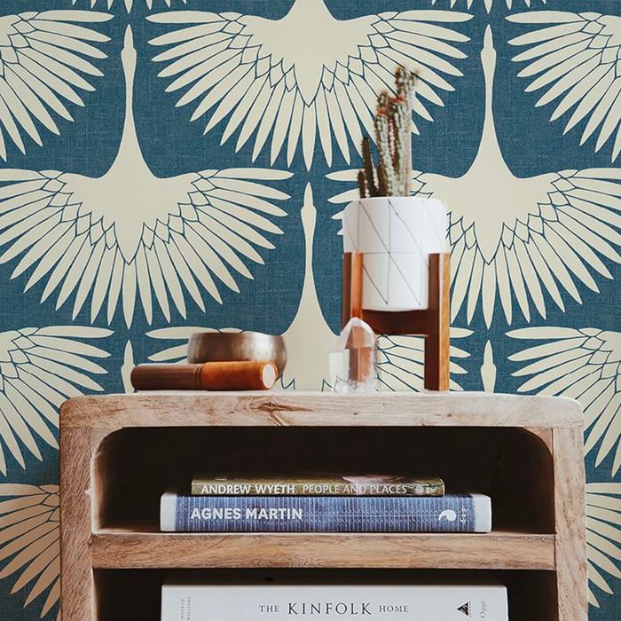A wooden shelf displays books and decorative items. Above, a patterned wall showcases white cranes on a blue background, enhancing the cozy interior atmosphere.