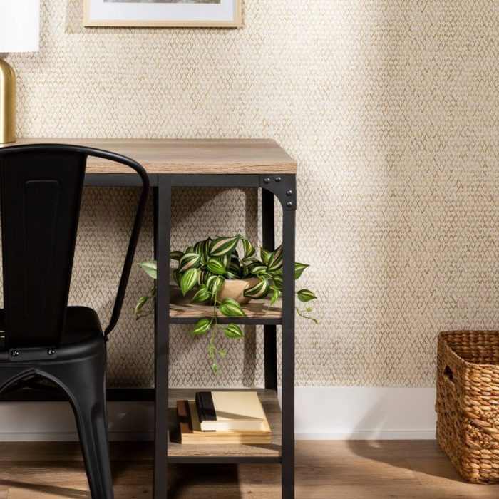 A black chair sits next to a wooden desk, which has a potted plant below. A woven basket rests on the floor nearby.