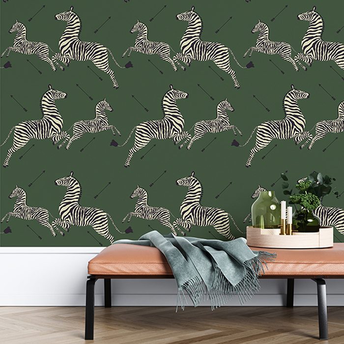 Black-and-white zebras are illustrated in various jumping poses against a dark green background, while a minimalist bench in the foreground holds decorative items.