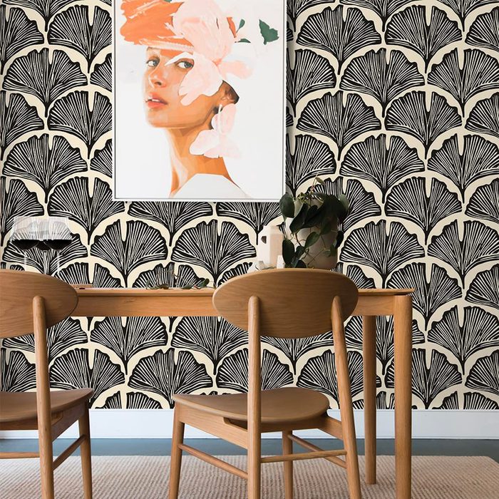A wooden table with two chairs sits in front of a patterned wall. Above, a framed portrait features a woman adorned with flowers.