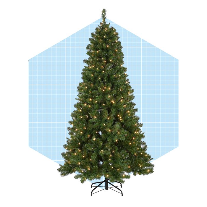 A decorated Christmas tree stands upright, illuminated with warm lights, against a light blue grid-patterned background, suggesting a festive atmosphere.