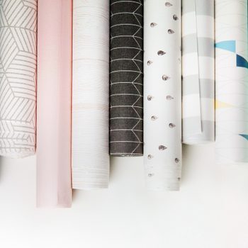Rolls of decorative wallpaper are arranged vertically, showcasing various colors and patterns against a neutral background.