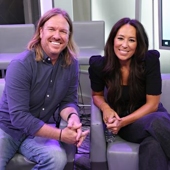 Two smiling individuals sit together on modern gray chairs in a well-lit indoor space, with a screen visible in the background.