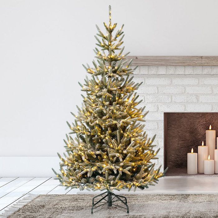 A decorated Christmas tree stands illuminated beside a brick fireplace, with flickering candles arranged on the hearth, enhancing a cozy, festive atmosphere.