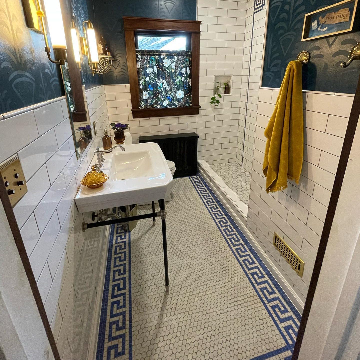 A vintage-style sink stands against tiled walls. A towel hangs nearby as natural light filters through a floral curtain, illuminating the room's decor.