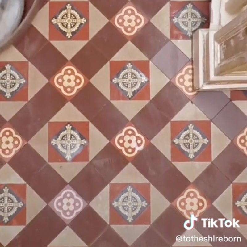 A patterned tiled floor features alternating red and beige diamond shapes, with floral motifs at intersections, suggesting a vintage or decorative interior space.