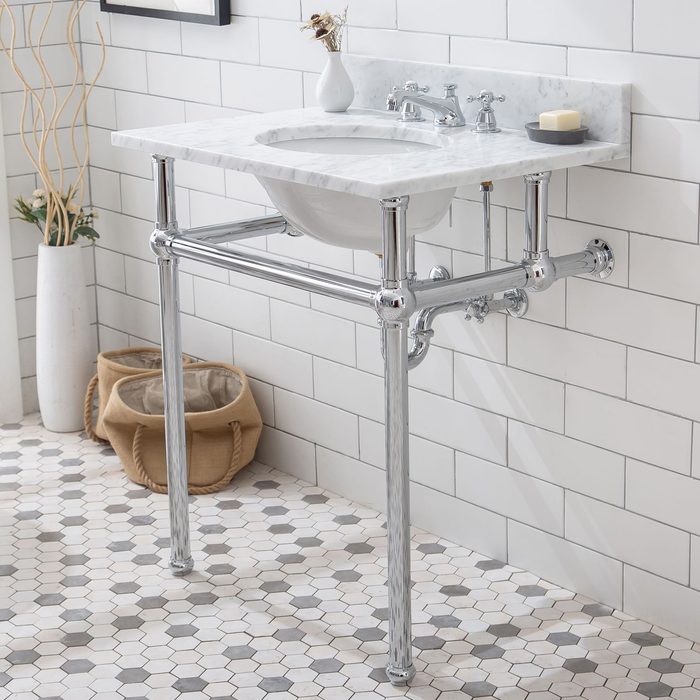 A chrome faucet and sink are mounted on a marble countertop, supported by sleek legs, in a clean bathroom with hexagonal tiled flooring.