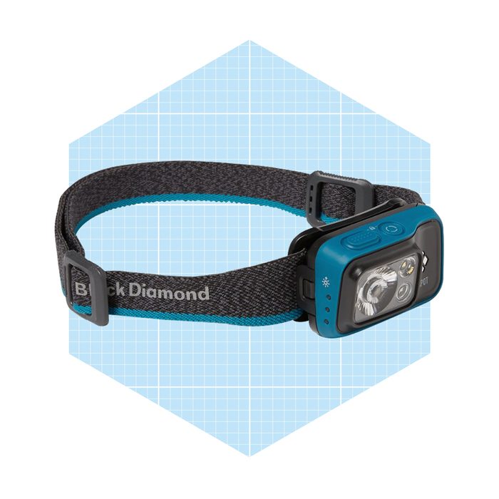 A headlamp rests on a patterned background, designed for hands-free lighting, featuring a dark strap with a blue accent and a control panel on one side.