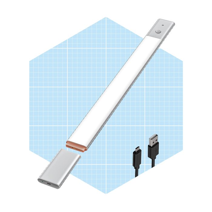 A sleek, LED light bar rests on a grid-patterned background, with a removable power bank and USB cables nearby, suggesting a modular lighting solution.