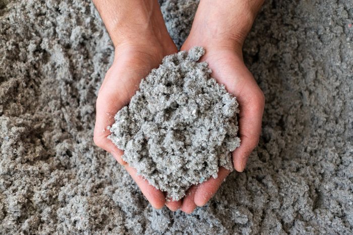 Hands hold a mound of gray, fluffy material, while a similar texture covers the surrounding surface, suggesting a soft, powdery substance.