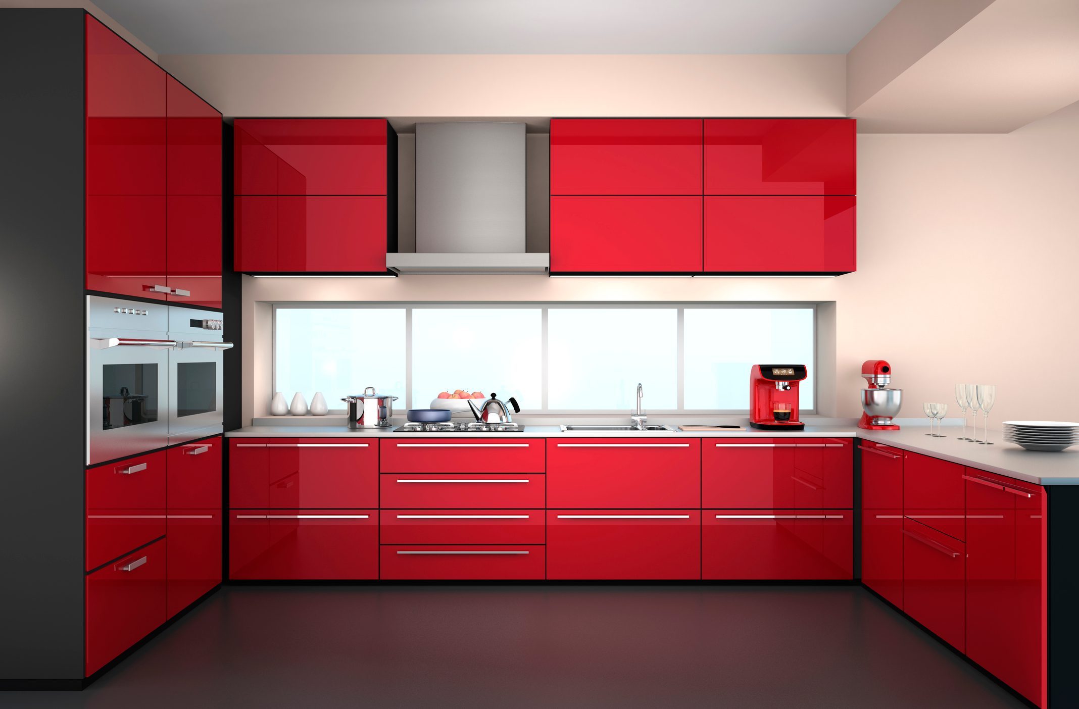 A modern kitchen features sleek red cabinetry, a stainless steel stove, and countertop appliances, illuminated by natural light from a large window.