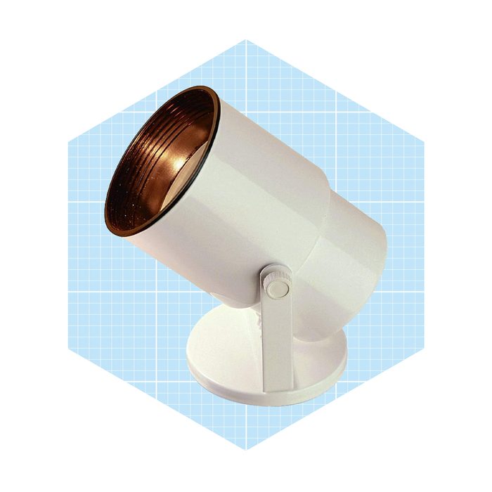 A white spotlight rests on a circular base, angled upward, showcasing a metallic inner finish against a light blue, grid-patterned background.