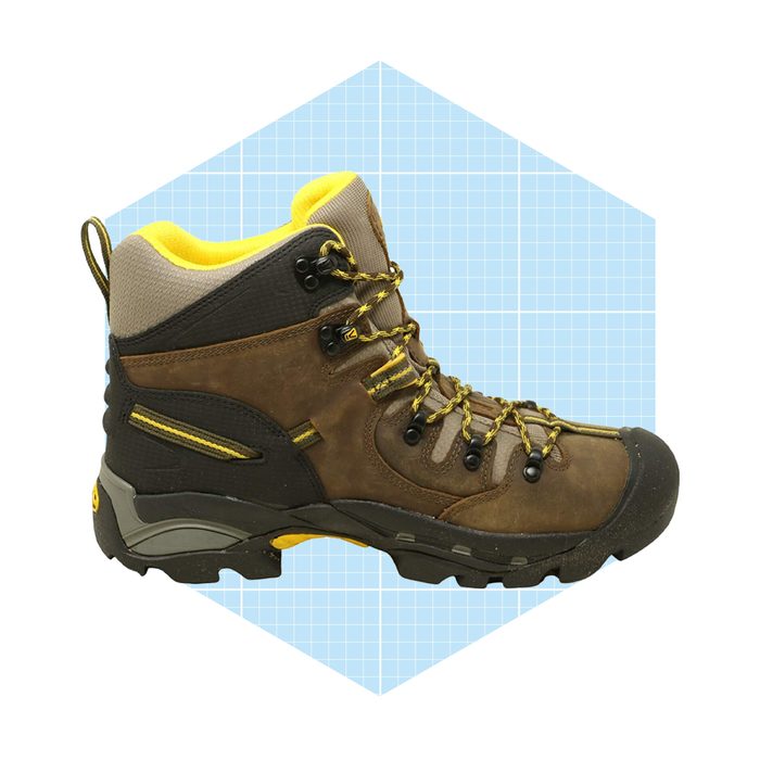 A hiking boot stands upright with a brown and yellow design, showcasing reinforced areas and laces against a light blue geometric background.