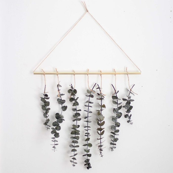 Hanging eucalyptus branches decorate a horizontal rod, suspended by twine against a light-colored wall, adding a natural touch to the environment.