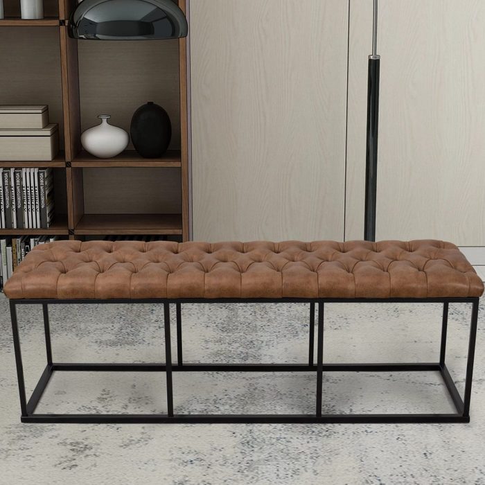 A tufted brown leather bench rests on a patterned floor, surrounded by wooden shelves displaying decor and books, enhancing a contemporary interior space.