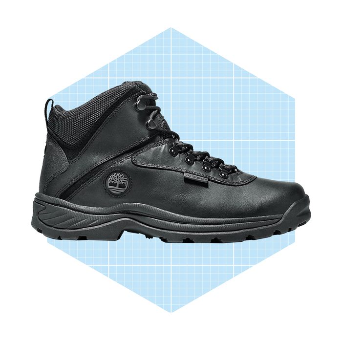 A black hiking boot stands upright, displaying laces and a textured design, set against a light blue grid hexagonal background.