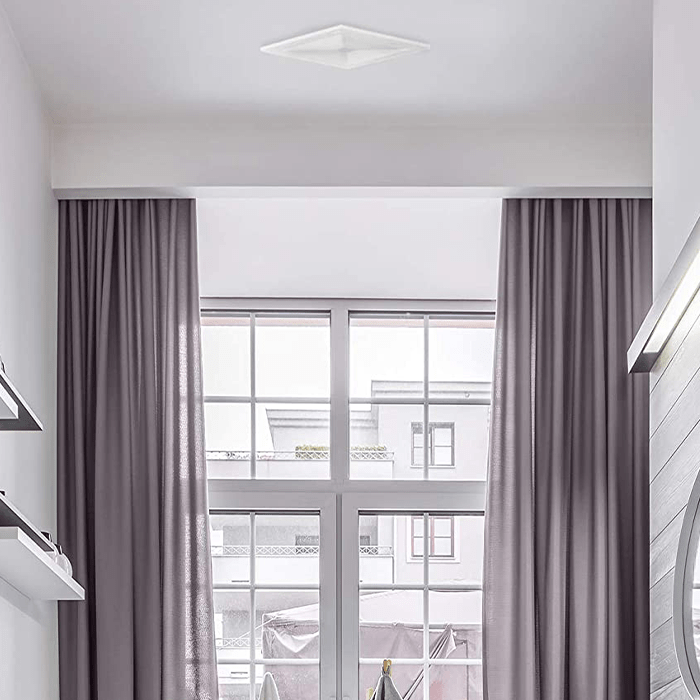 A ceiling light illuminates a modern room with large windows, flanked by long, gray curtains, revealing an urban view outside.