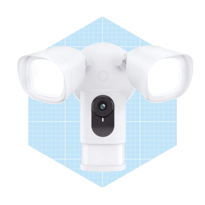 A security light with dual adjustable floodlights and a central camera is positioned against a light blue grid background, designed for monitoring and illumination.