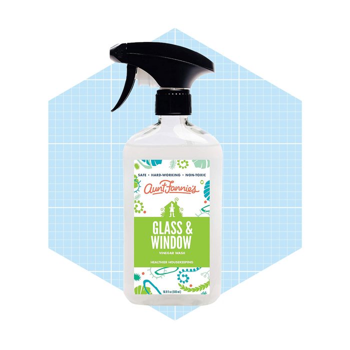 A spray bottle of glass and window cleaner is displayed, highlighting its non-toxic formula against a light blue geometric background.