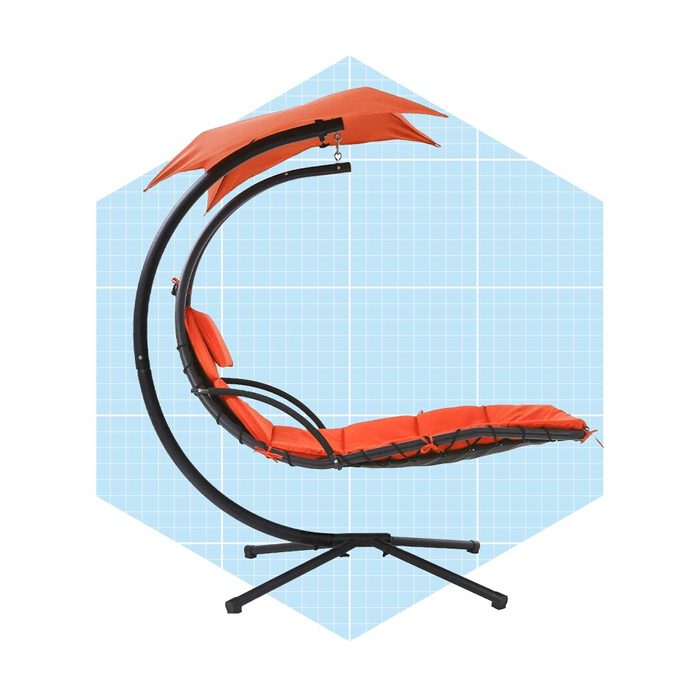 A bright orange hanging chair sways gently, suspended by a curved black frame, set against a light blue, grid-patterned background.