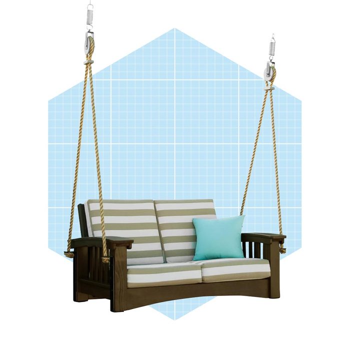 A wooden swing sofa with striped upholstery sits suspended by ropes against a light blue grid-patterned background, featuring a turquoise pillow on one side.