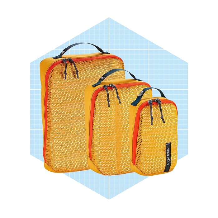 Three yellow packing cubes display zippers and handles, arranged in ascending size. They stand against a light blue, grid-patterned background.