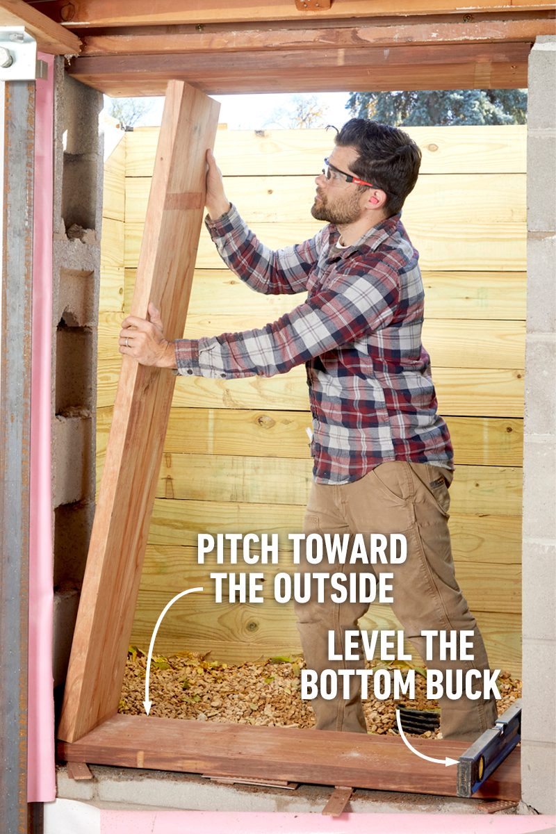 A man holds a wooden board while adjusting its position inside a building, with a rustic wooden backdrop and a level tool nearby for alignment.