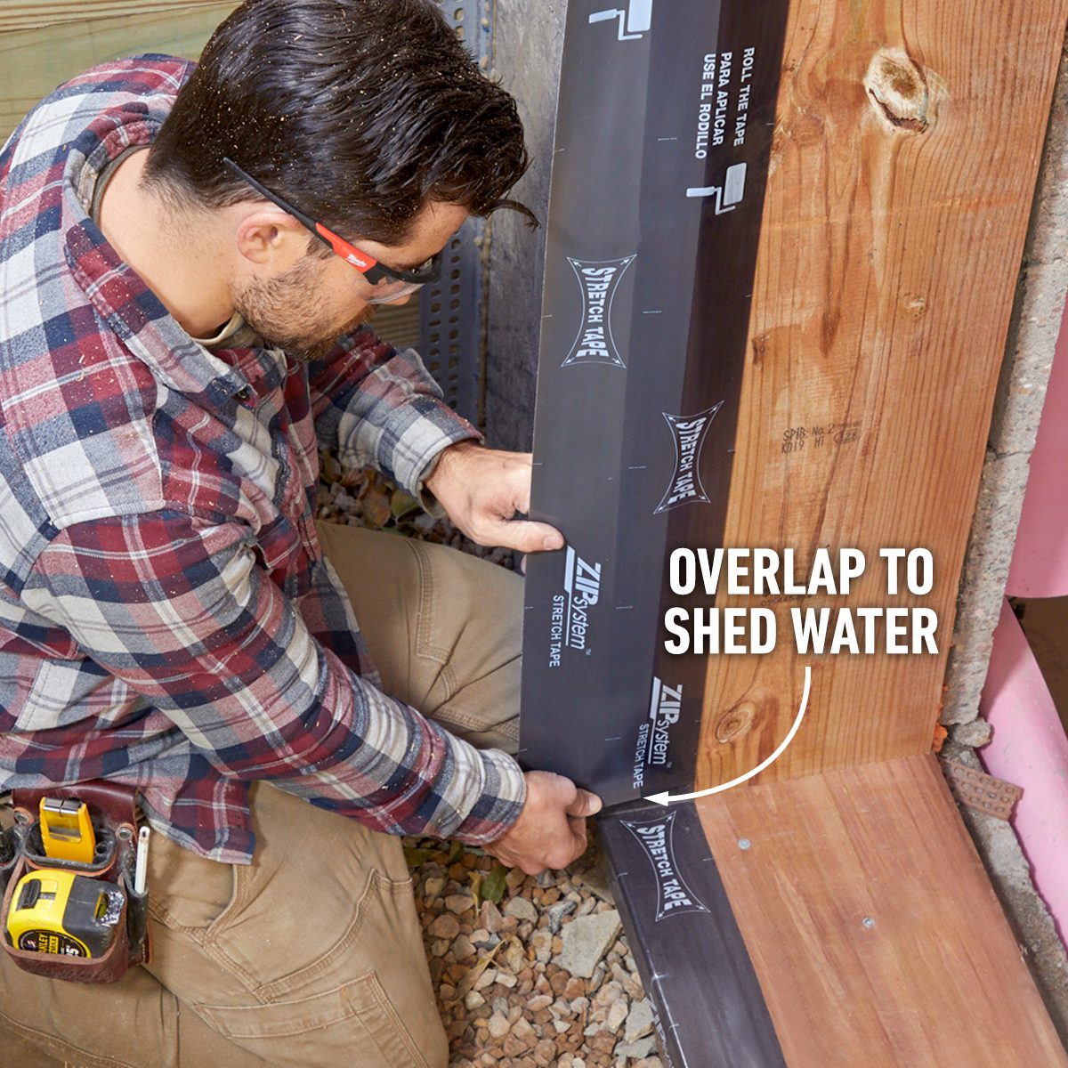 A man applies a waterproof membrane to a wooden structure, ensuring proper overlap to direct water away, surrounded by gravel and construction materials.