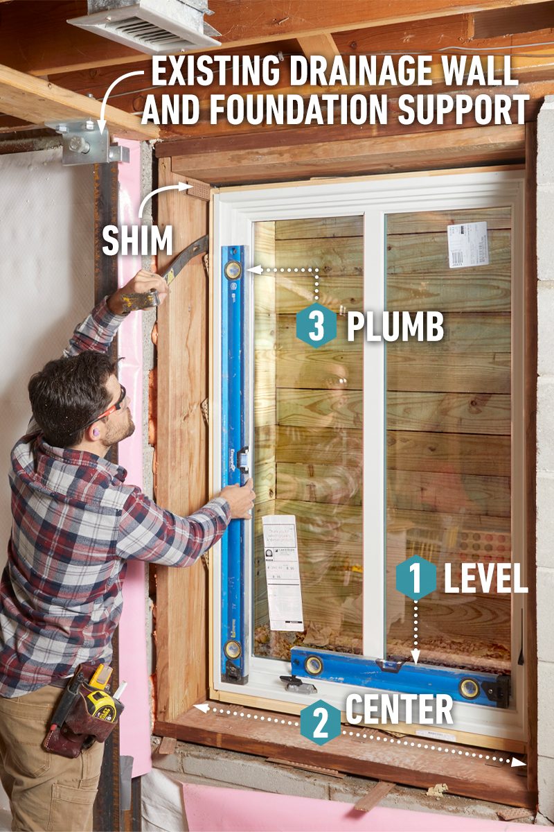 A person uses a level on a window frame to ensure it is plumb and centered, set against a backdrop of exposed walls and beams.
