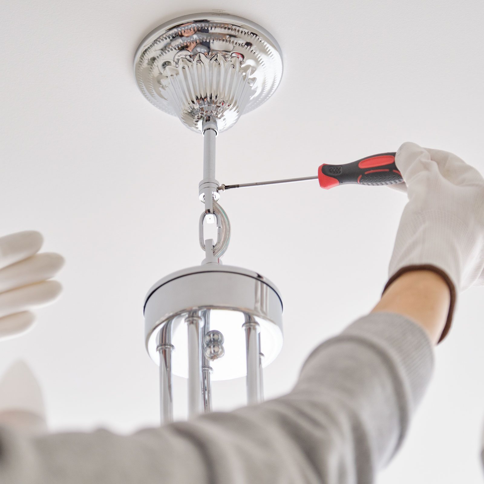 Hands Of Electrician installing a chandelier with professional tools