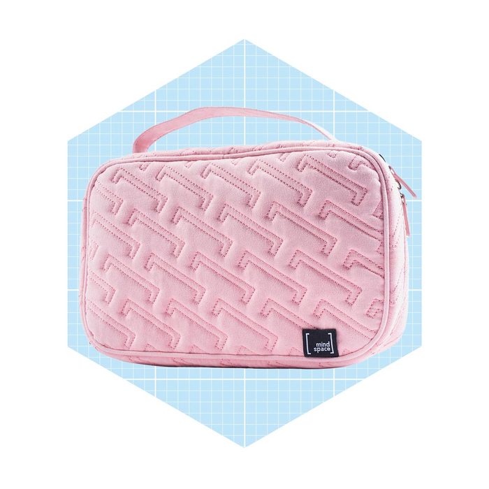 A pink quilted cosmetic bag rests on a light blue grid background, showcasing a sleek design and a carry handle for portability.