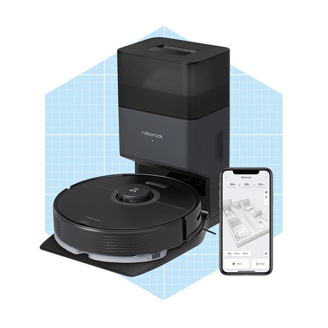 A robot vacuum sits on a dock, connected to a smartphone displaying a floor plan, designed for automated cleaning in a modern workspace.