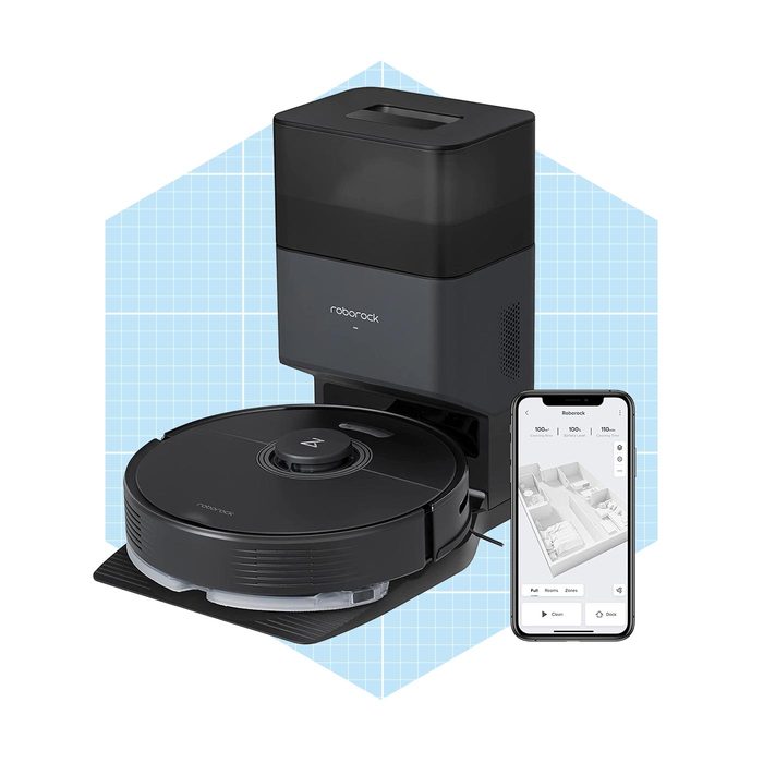 A robot vacuum sits on a dock, connected to a smartphone displaying a floor plan, designed for automated cleaning in a modern workspace.